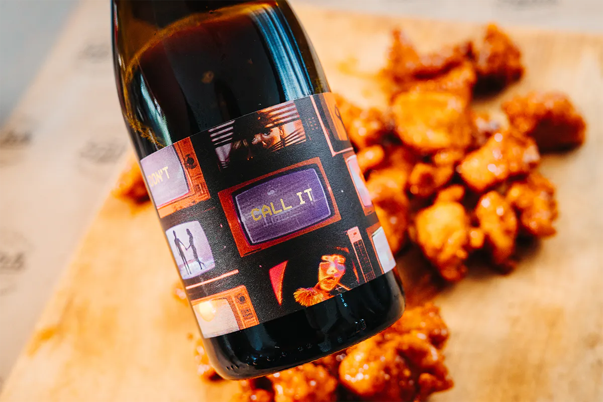 A wine bottle with chicken bites in the background.